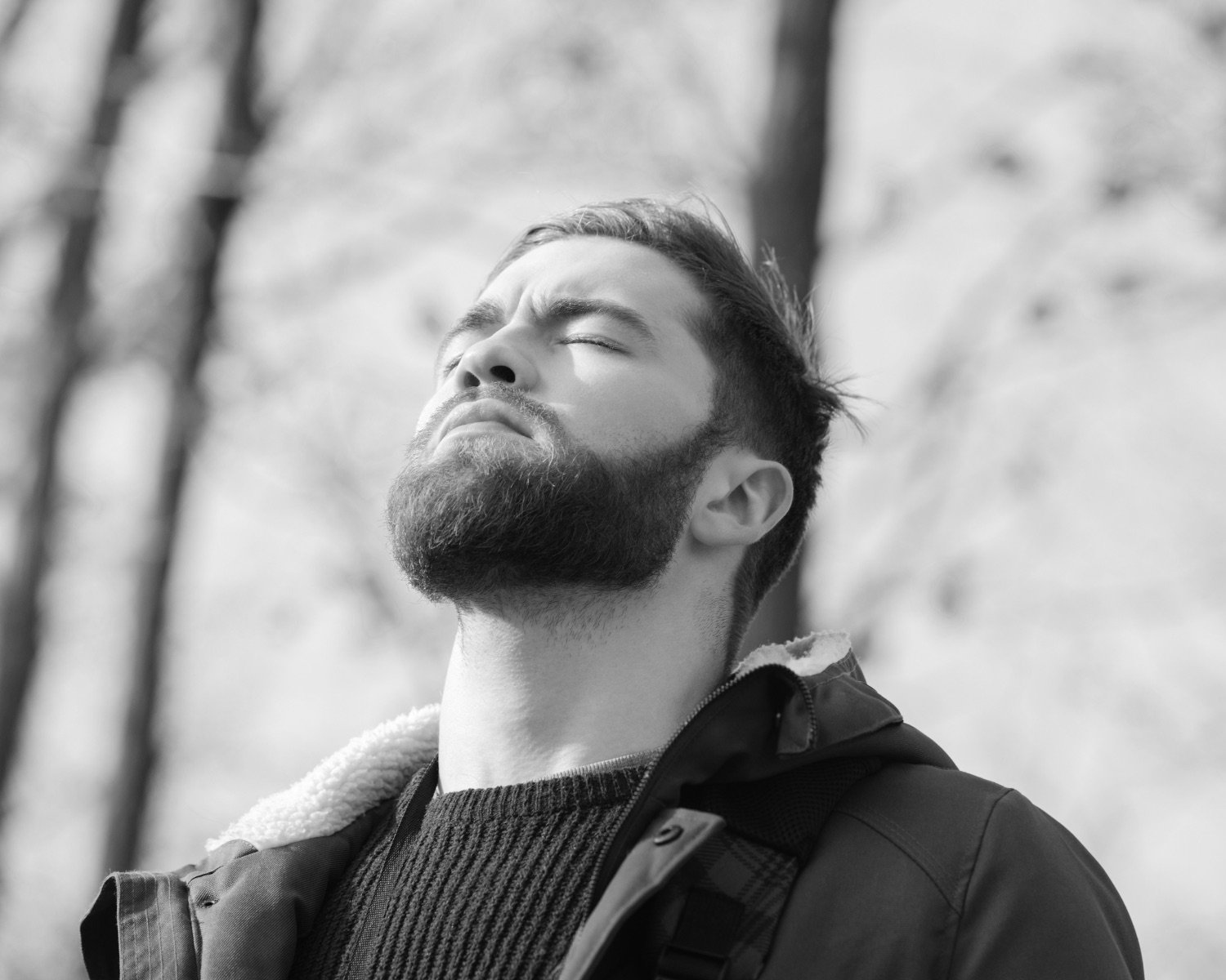 A man standing outdoors, eyes closed, breathing in with the sun on his face
